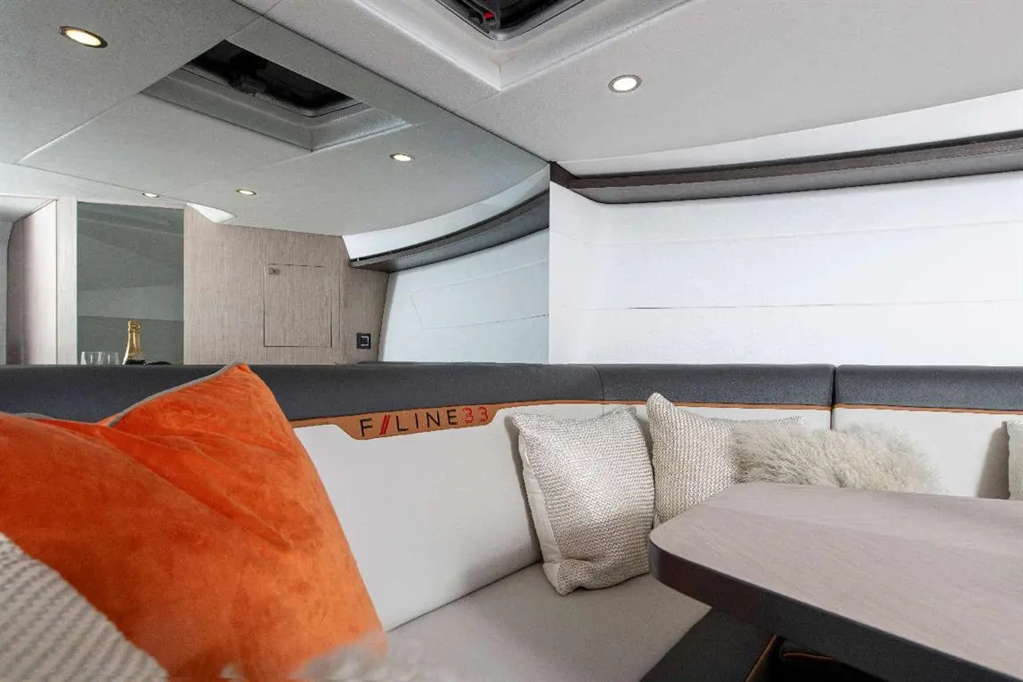 Modern yacht interior featuring a grey and white seating area with cushions, a wooden table, and a champagne bottle in the background.